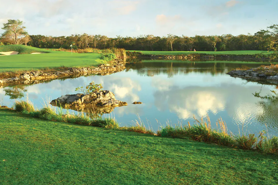 A lake edged with limestone beside a green at El Tinto Golf Course in Cancún