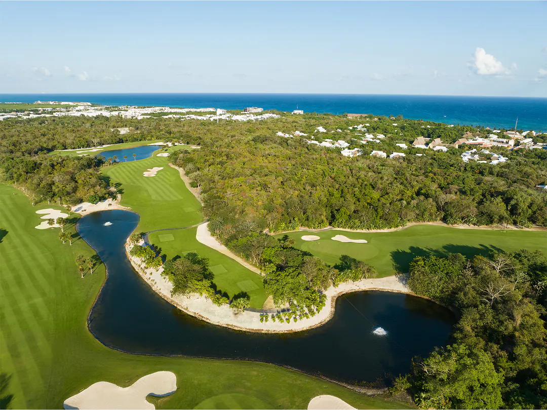 Aerial view of Gran Coyote Golf in the Riviera Maya: fairways and a lake winding through the jungle, with the Caribbean Sea beyond